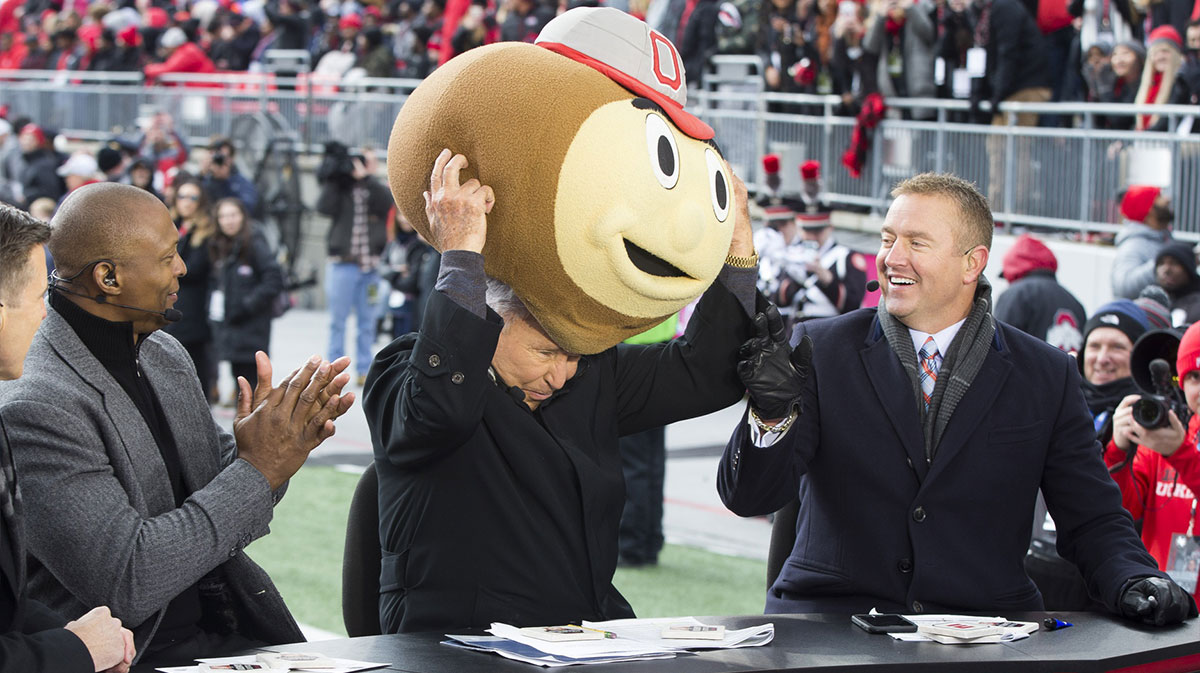 ESPN Gameday host Lee Corso puts on a Brutus Buckeye head on while sitting between former Buckeyes Eddie George and Kirk Herbstreit before the game between the Ohio State Buckeyes and Penn State Nittany Lions at Ohio Stadium.