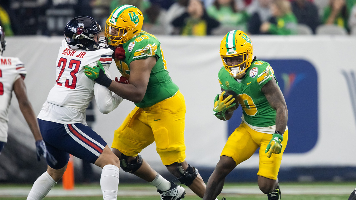 Oregon Ducks running back Bucky Irving (0) runs the ball as offensive lineman Ajani Cornelius (65) blocks Liberty Flames college football transfer portal defensive end TJ Bush Jr. (23) during the 2024 Fiesta Bowl at State Farm Stadium.
