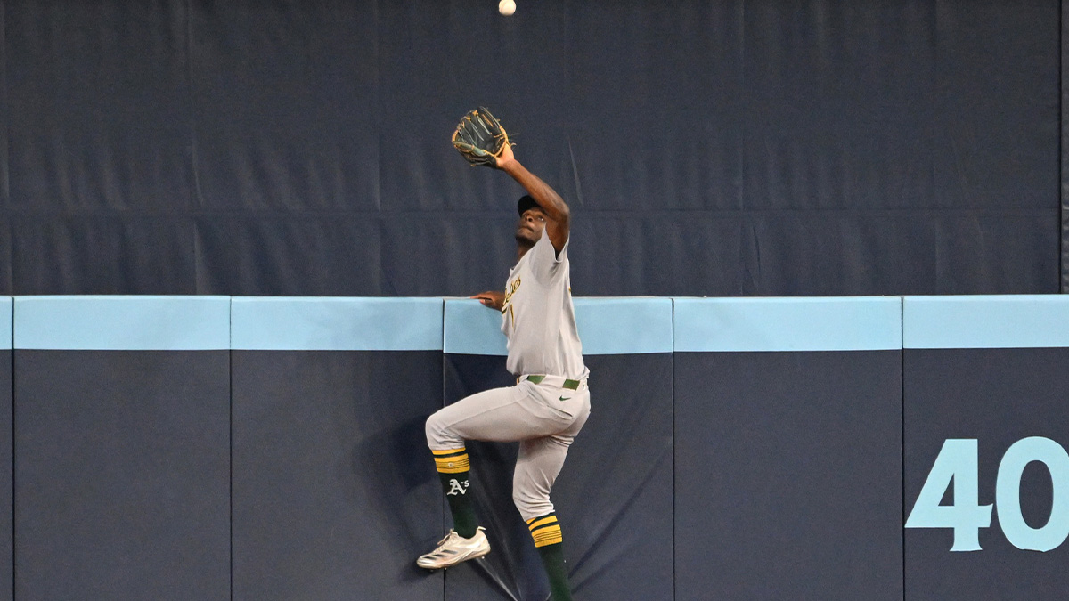 Athletics center fielder Denzel Clarke (1) climbs the outfield wall to catch a fly ball hit by Toronto Blue Jays catcher Alejandro Kirk (not shown) in the fifth inning at Rogers Centre.