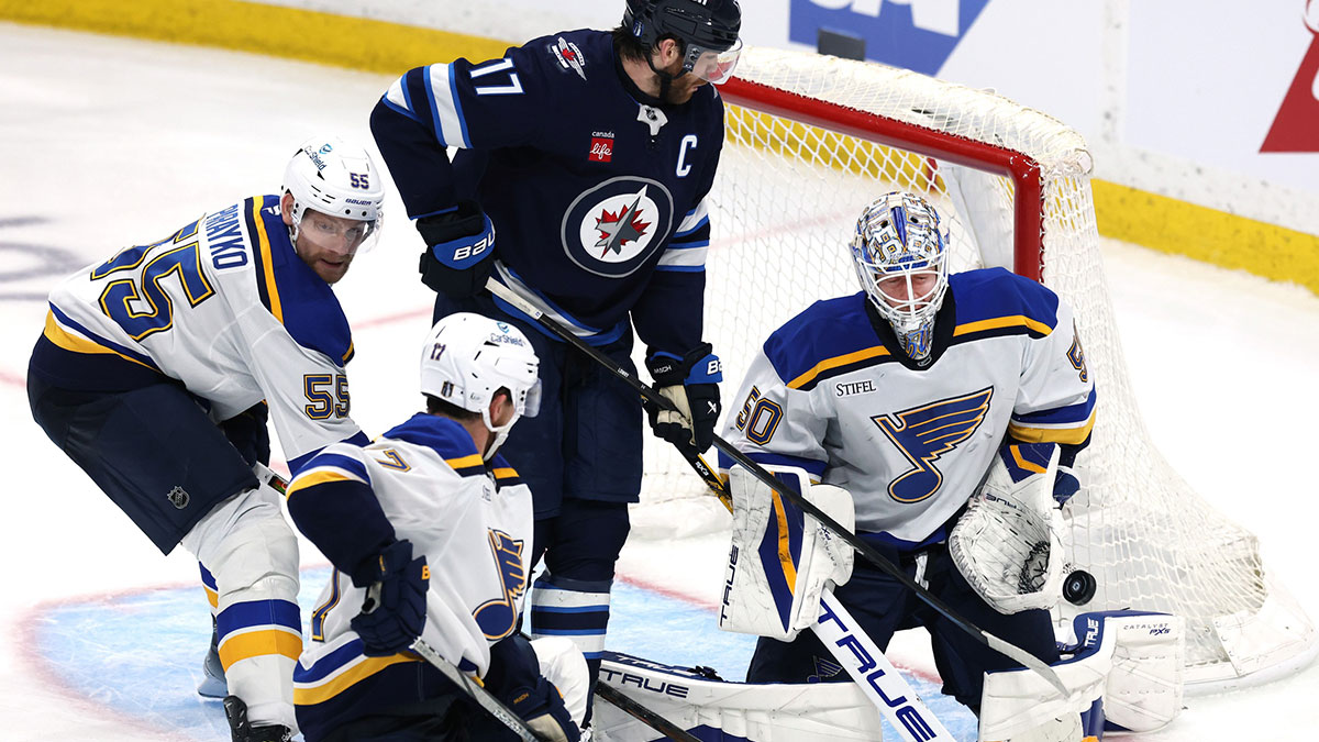 St. Louis Blues goaltender Jordan Binnington (50) makes a save as Winnipeg Jets center Adam Lowry (17) looks for a rebound in the first overtime in game seven of the first round of the 2025 Stanley Cup Playoffs at Canada Life Centre.
