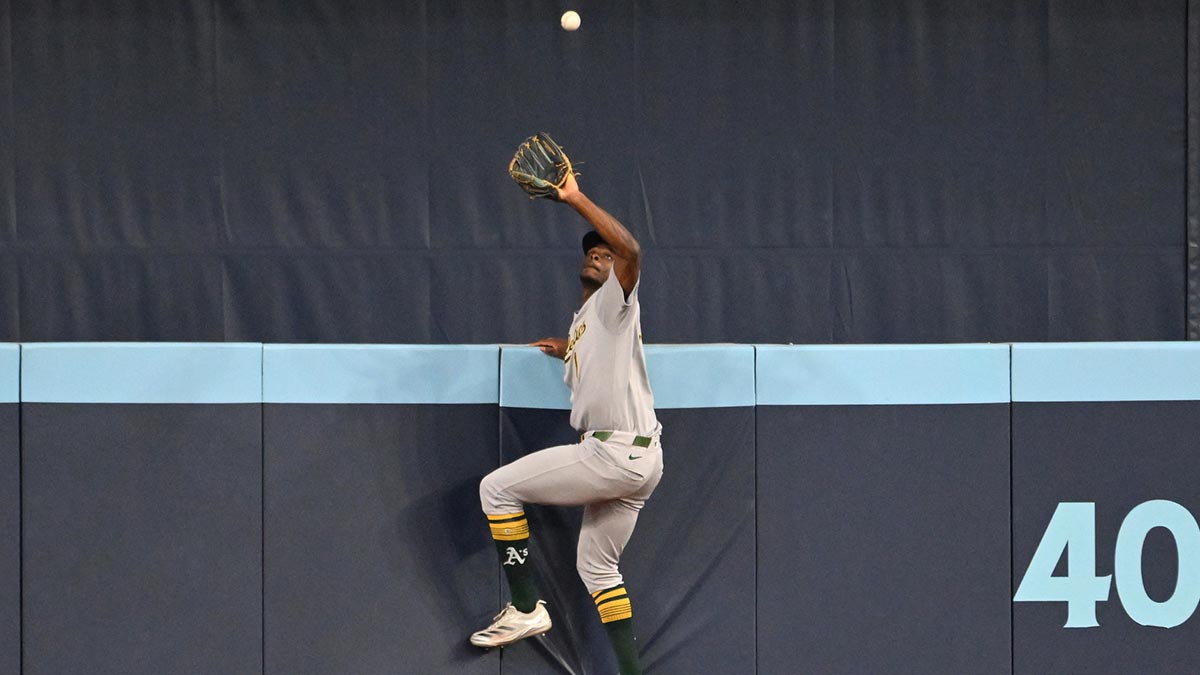 Athletics center fielder Denzel Clarke (1) climbs the outfield wall to catch a fly ball hit by Toronto Blue Jays catcher Alejandro Kirk (not shown) in the fifth inning at Rogers Centre.
