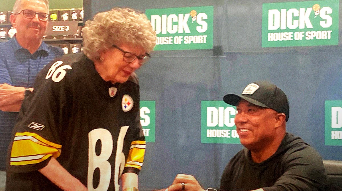 Former Pittsburgh Steelers receiver and Super Bowl MVP Hines Ward signs a card for Erie resident Melanie Hoitinga, who was the first person in line for Ward's Aug. 19, 2023, autograph session at Dick's Sporting Goods reopening within the Millcreek Mall.
