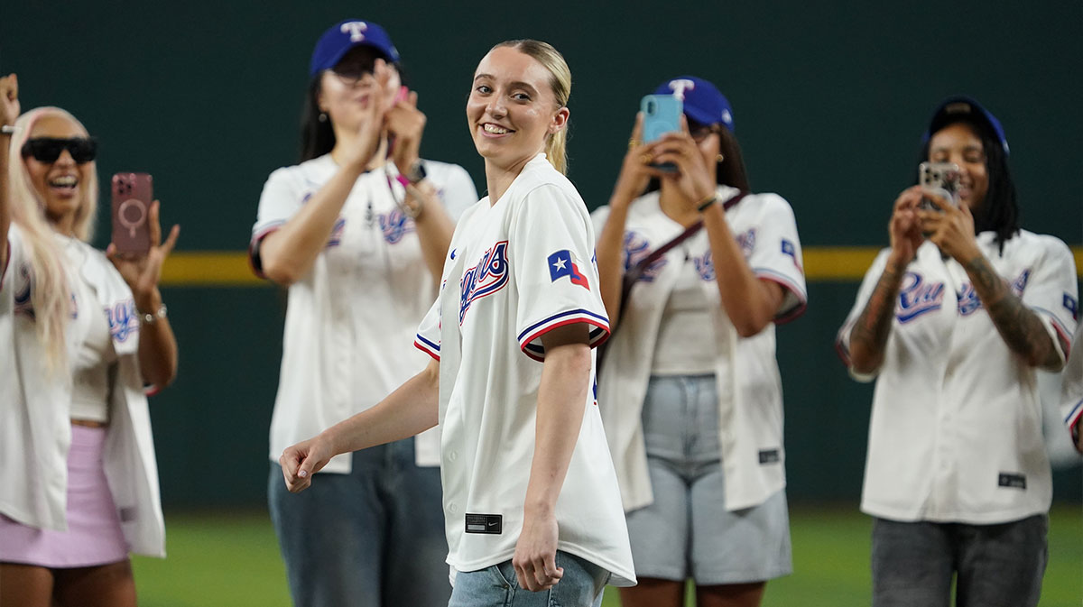 Dallas Wings point guard Paige Bueckers reacts after throwing out the first pitch, with her teammates in the background prior to game between the Texas Rangers and the Kansas City Royals at Globe Life Field.