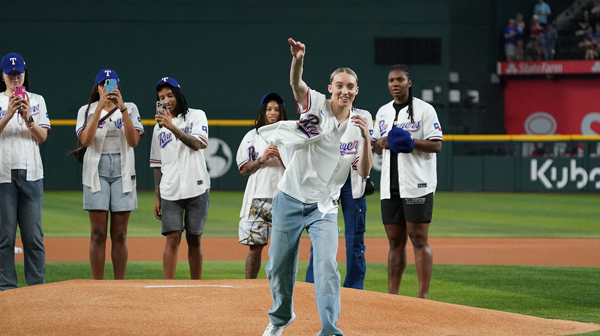 Dallas Wings point guard Paige Bueckers throws out the first pitch with her teammates in the background prior to game between the Texas Rangers and the Kansas City Royals at Globe Life Field.