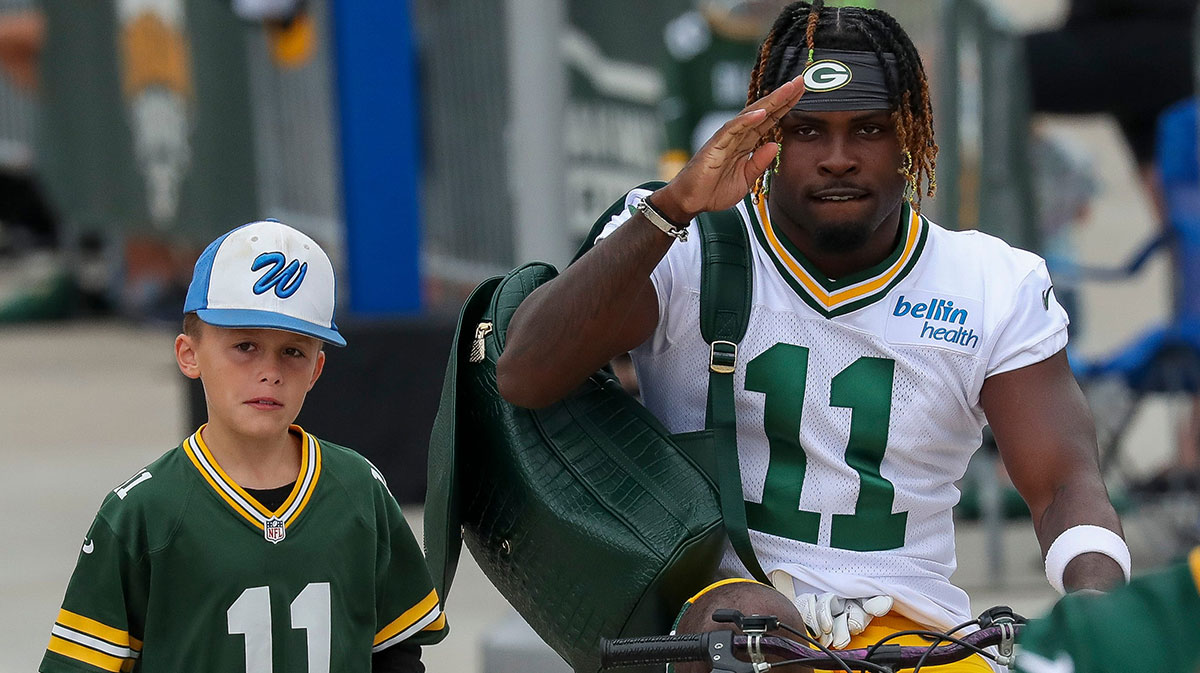 Green Bay Packers wide receiver Jayden Reed (11) salutes to the crowd as he rides a young fan’s bicycle in the DreamDrive before practice on Tuesday, July 23, 2024, at Lambeau Field in Green Bay, Wis.