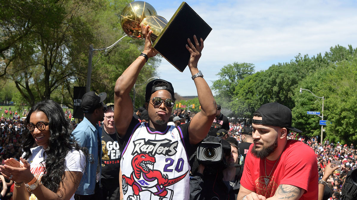 Toronto Raptors guard Kyle Lowry hoist the Larry O'Brien trophy to fans in the company of his wife Ayahna (left) and guard Fred VanVleet (right) during a parade through downtown Toronto to celebrate their NBA title.