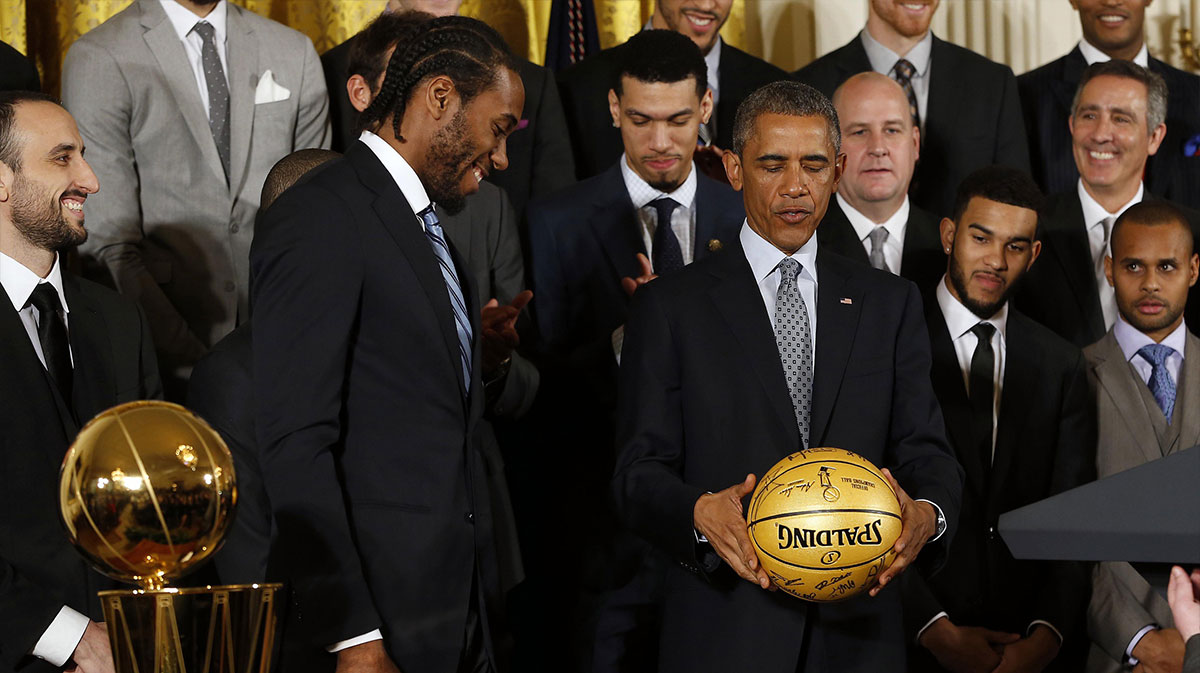 San Antonio Spurs striker Kawhi Leonard (left), presents President Barack Obama (right) with a ball signed by Spurs during a ceremony honoring the NBA Spurs in the east house of the White House.