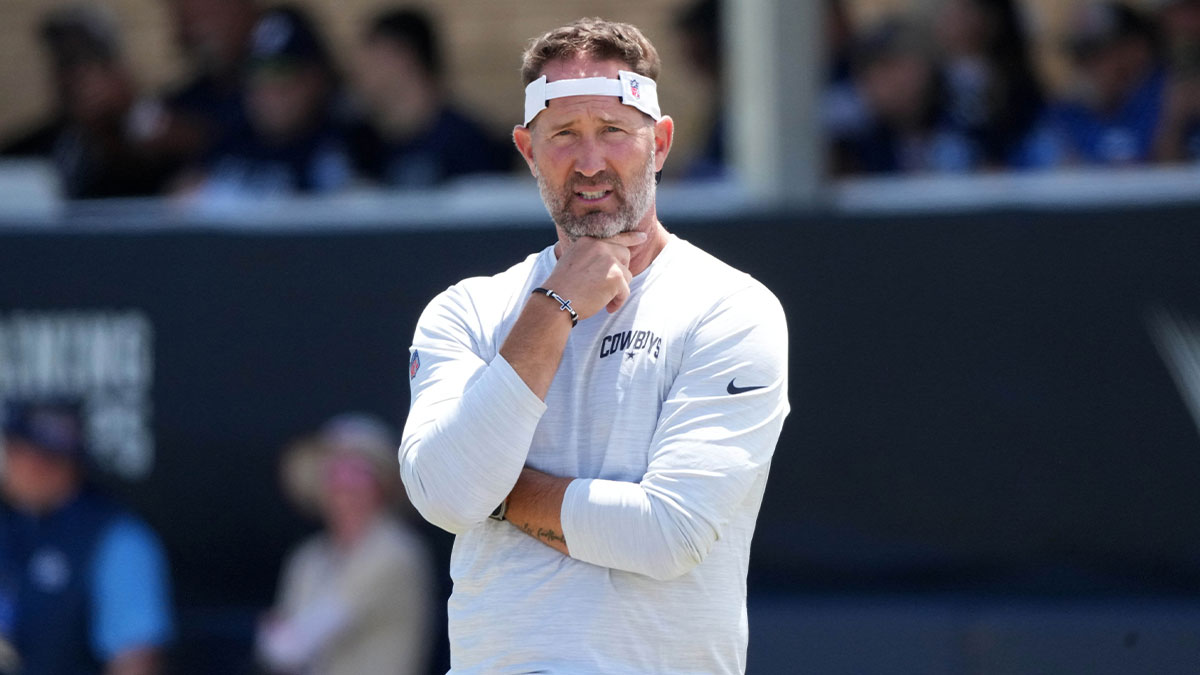 Cowboys coach Brian Schottenheimer at training camp at the River Ridge Fields with Fox Sports 1's Colin Cowherd in the background