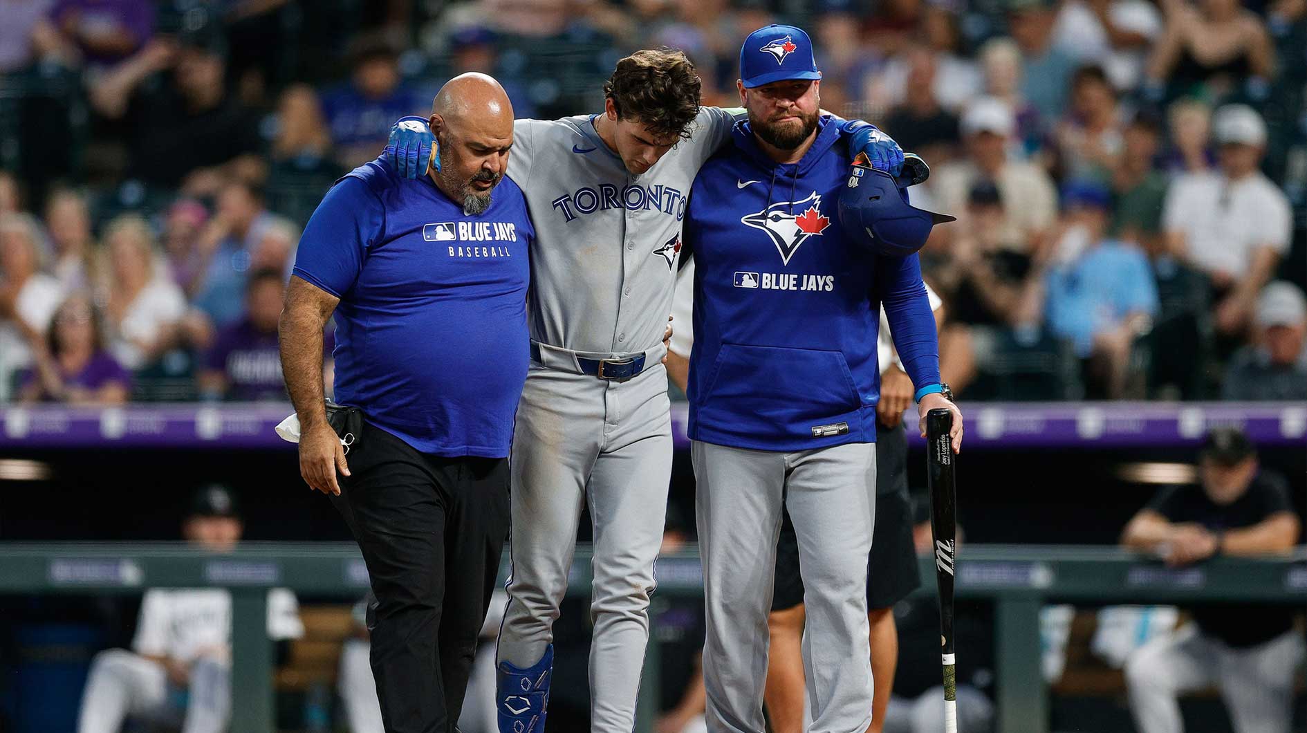 Toronto Blue Jays left fielder Joey Loperfido (C) is helped off the field by head athletic trainer Jose Ministral (L) and manager John Schneider (R) in the sixth inning against the Colorado Rockies at Coors Field.