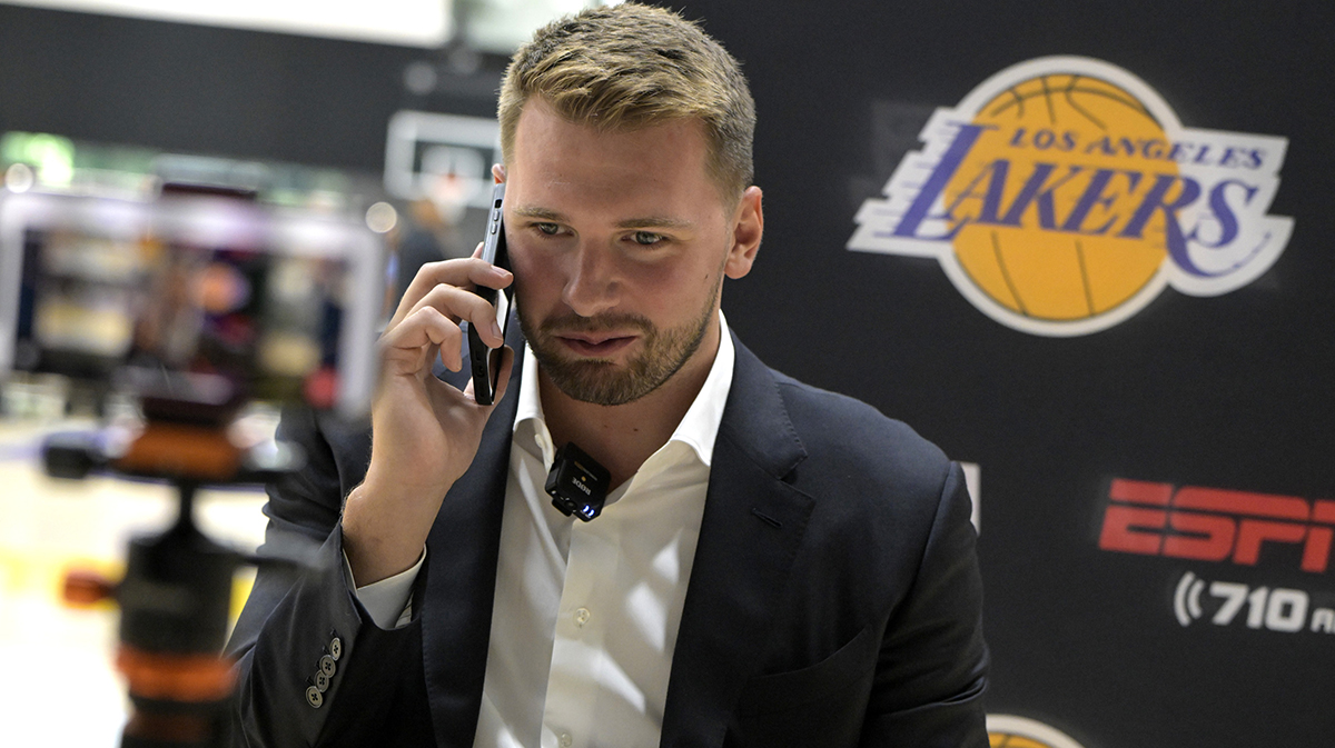 Lakers Luka Doncic (77) is interviewed by ESPN LA radio following a press conference announcing the signing of a 3-year, $165 million contract extension at UCLA Health Training Center with the Slovenia flag in the background