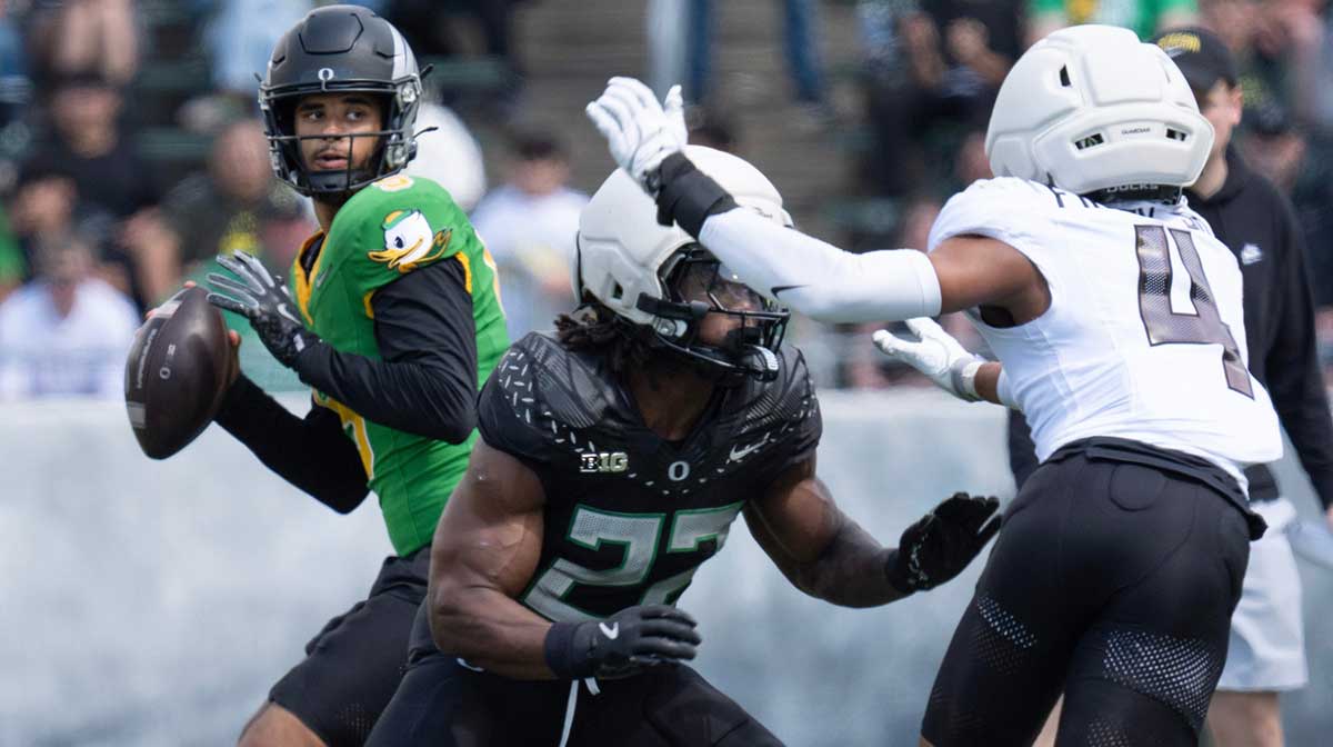 Combat Duck Dante Moore, left, drops back to pass behind a block by Jay Harris against Fighting Duck Brandon Finny during the fourth quarter of the Oregon Spring Game.