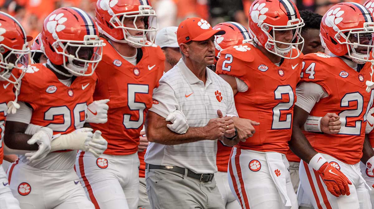 Clemson head coach Dabo Swinney arm-in-arm with defensive back Ronan Hanafin (5) and quarterback Cade Klubnik (2) and teammates during the “Walk of Champions” march to the end zone, before the game with Clemson and Louisiana State University at Memorial Stadium in Clemson, S.C. Saturday, August 30, 2025.