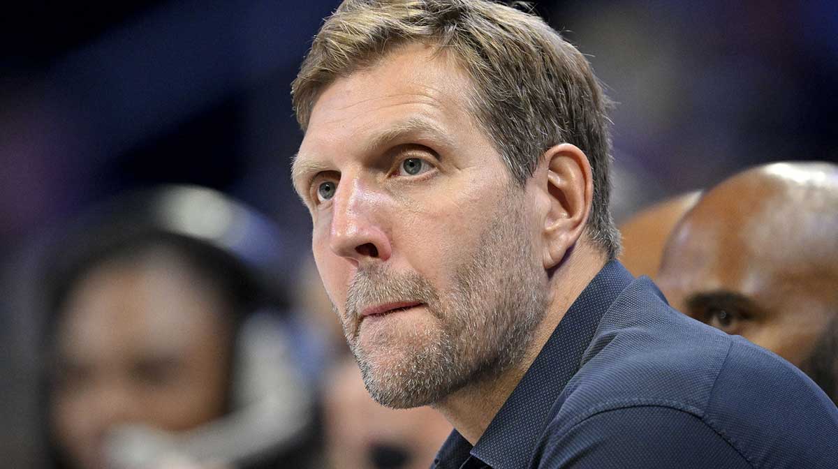 Dirk Nowitzki watches the game between the Dallas Wings and the Seattle Storm during the first half at College Park Center with the 2025-26 Mavericks in the background