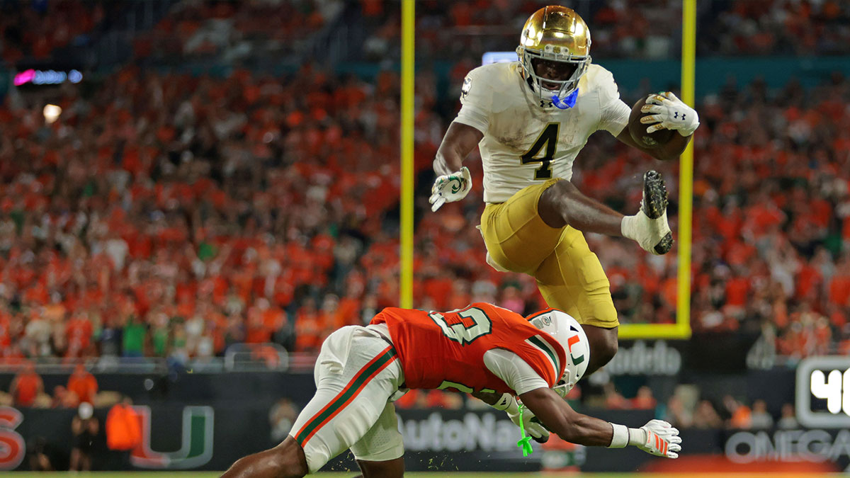 Notre Dame Fighting Irish running back Jeremiyah Love (4) hurdles over Miami Hurricanes defensive back Dylan Day (23) during the third quarter at Hard Rock Stadium.