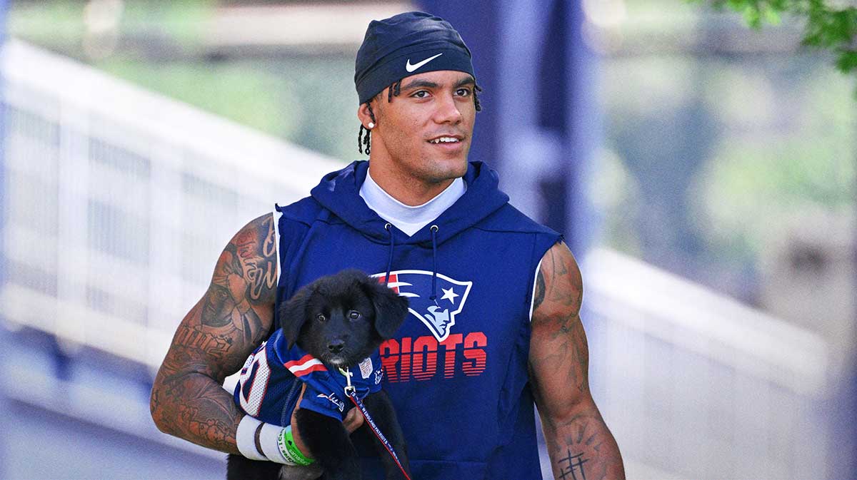 New England Patriots cornerback Christian Gonzalez (0) delivers a puppy to a local family as part of the Patriots pet adoption event before training camp at Gillette Stadium.