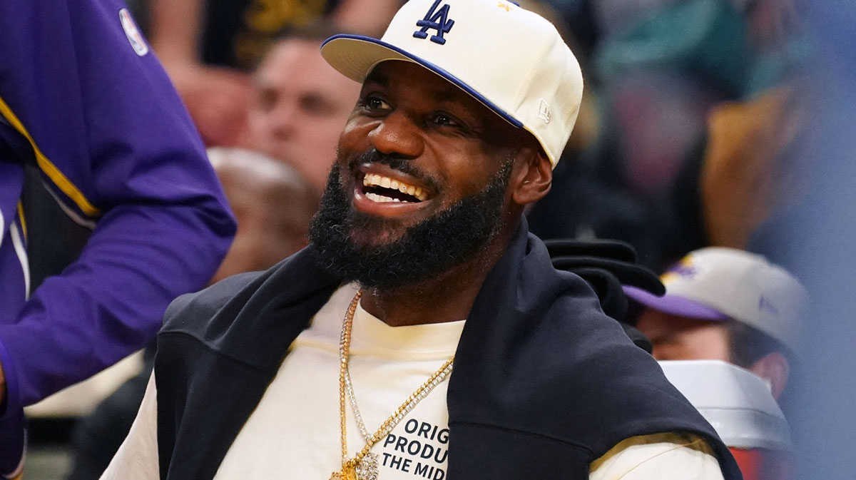 Los Angeles Lakers forward LeBron James (23), wearing a Los Angeles Dodgers hat, smiles after watching his son, guard Bronny James (9), dunk a rebound against the Golden State Warriors in the third quarter at Chase Center.