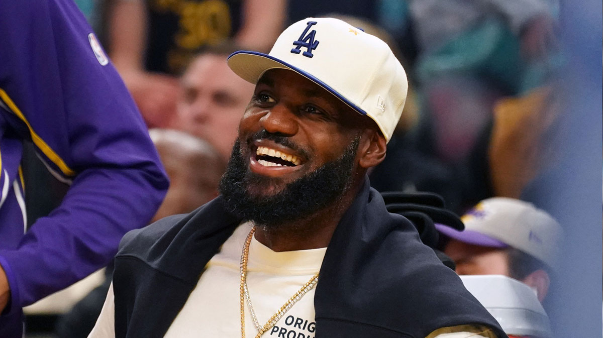 Lakers forward LeBron James (23), wearing a Los Angeles Dodgers hat, smiles after watching his son, guard Bronny James (9), dunk a rebound against the Golden State Warriors in the third quarter at Chase Center