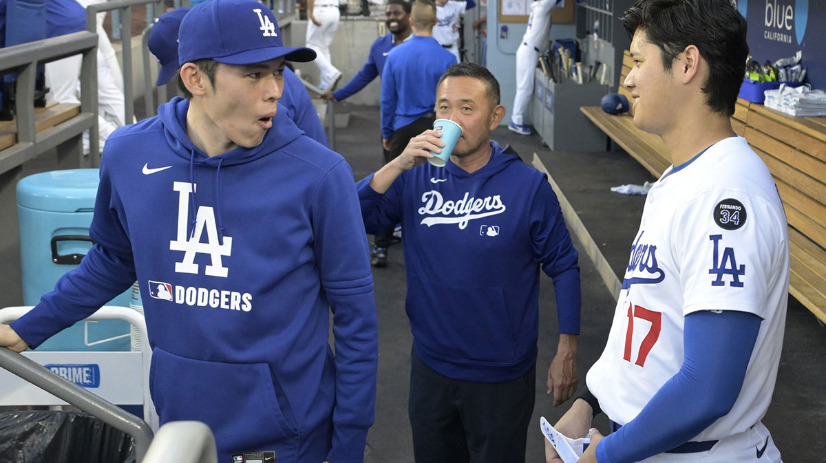 Los Angeles Dodgers designated hitter Shohei Ohtani (17) laughs with starting pitche Roki Sasaki (11) and trainer Yosuke Nakajima in the dugout prior to the game against the San Diego Padres at Dodger Stadium.