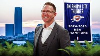 Thunder GM Sam Presti smiling with the Thunder's 2024-25 championship banner hanging in the background of an Oklahoma City skyline