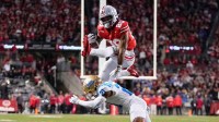 Ohio State Buckeyes running back James Peoples (20) hurdles UCLA Bruins defensive back Cole Martin (21) on his way to scoring a touchdown during the NCAA football game at Ohio Stadium in Columbus on Nov. 15, 2025.