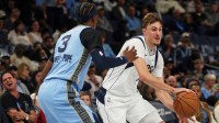 Mavericks forward Cooper Flagg (32) passes the ball against Memphis Grizzlies forward Kentavious Caldwell-Pope (3) during the third quarter at FedExForum with Hall of Fame forward Dirk Nowitzki in the background