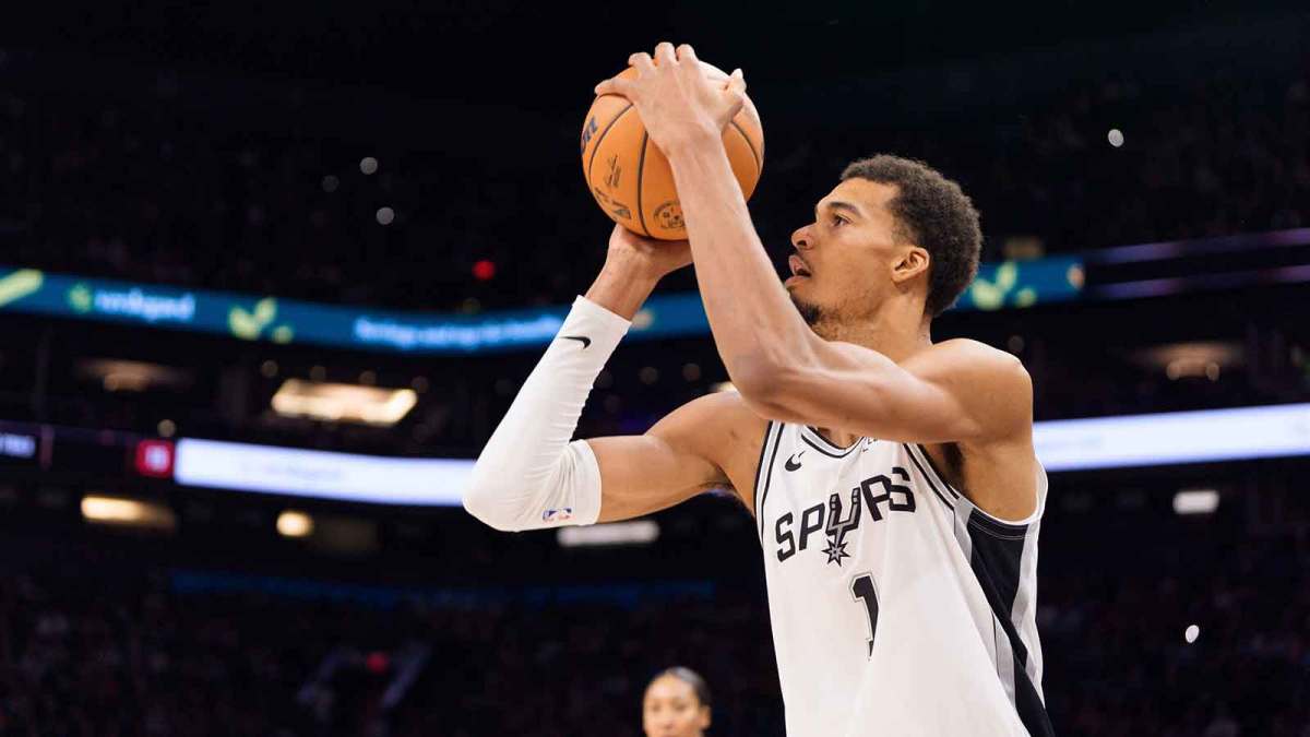 Spurs forward Victor Wembanyama (1) shoots a three pointer against the Phoenix Sun during the second half at Mortgage Matchup Center with Gilbert Arenas in the background
