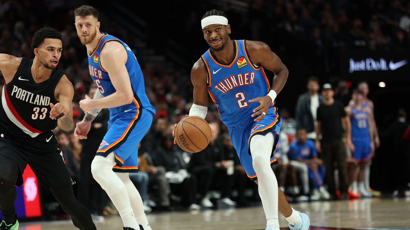 Thunder guard Shai Gilgeous-Alexander (2) dribbles the ball past Portland Trail Blazers forward Toumani Camara (33) as teammate Thunder’s center/forward Isaiah Hartenstein (55) watches during the first half at Moda Center