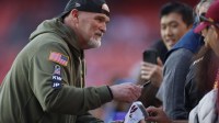 Washington Commanders head coach Dan Quinn signs autographs for fans on the sidelines prior to a game against the Detroit Lions at Northwest Stadium.