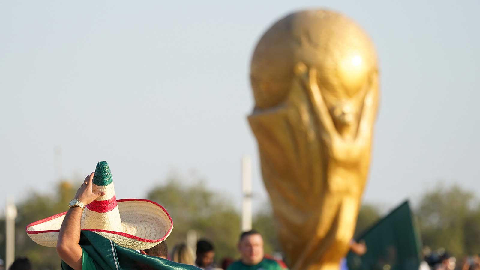 A Mexico fan wearing a sombrero walks past a World Cup trophy replica outside the stadium before the match against Poland during a group stage match at the 2022 World Cup at Ras Abu Aboud Stadium.
