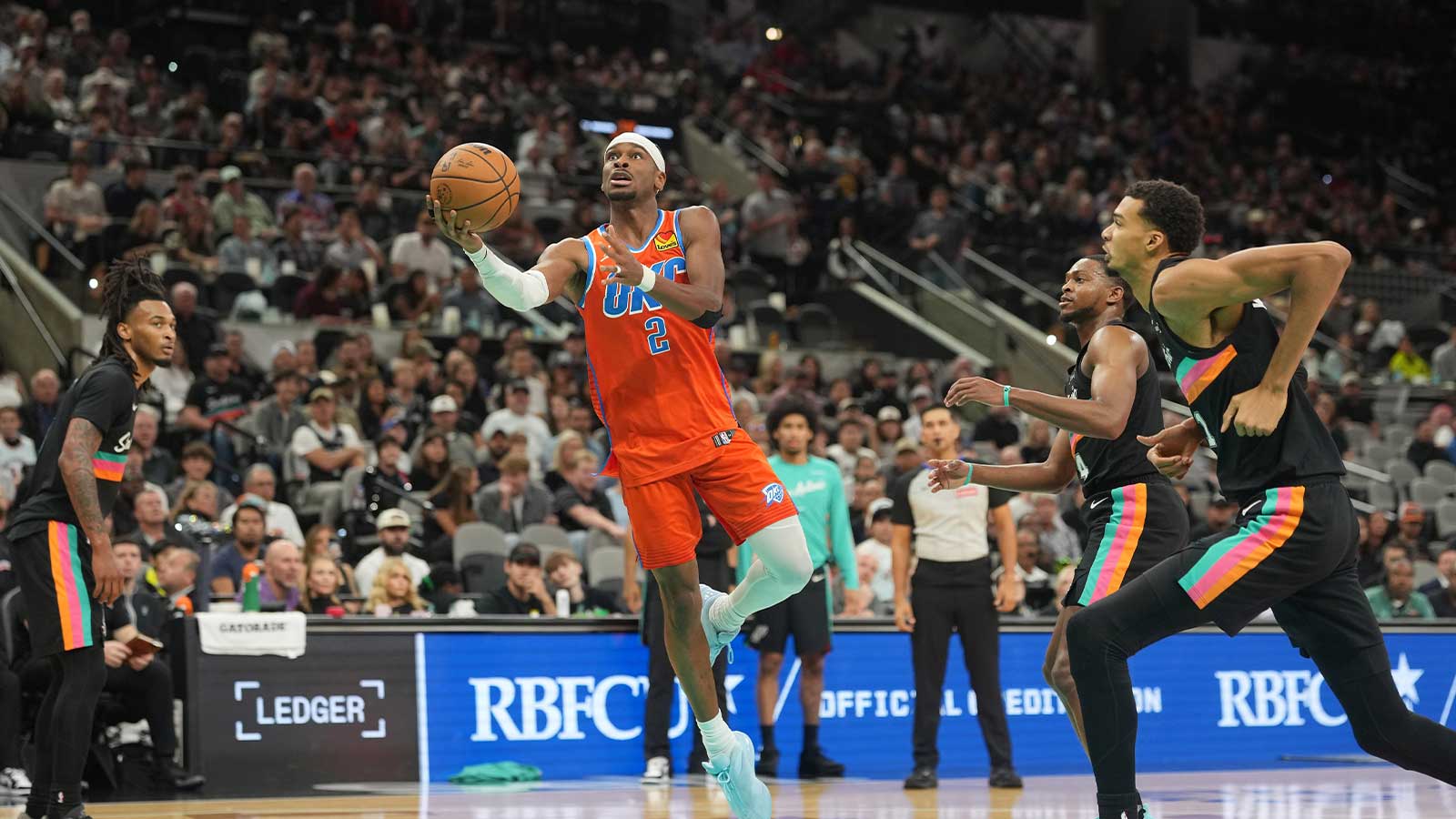 Thunder guard Shai Gilgeous-Alexander (2) drives to the basket between San Antonio Spurs forward Victor Wembanyama (1) and guard Stephon Castle (5) during the second half at Frost Bank Center