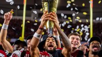 Indiana's Elijah Sarratt (13) lifts the trophy as Tyrique Tucker (95), Charlie Becker (80), Fernando Mendoza (15), and Mikail Kamara (6) celebrate on the podium after the College Football Playoff National Championship college football game at Hard Rock Stadium in Miami Gardens