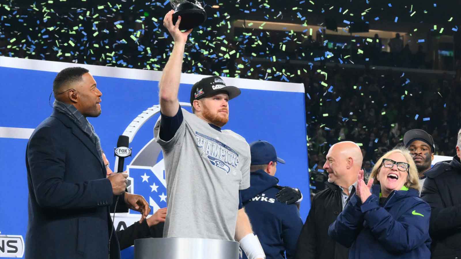 Seattle Seahawks quarterback Sam Darnold (14) celebrates with the trophy on the podium after defeating the Los Angeles Rams in the 2026 NFC Championship Game at Lumen Field.