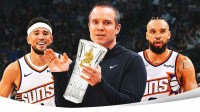 Phoenix Suns head coach Jordan Ott holding the NBA Coach of the Year award, along with Suns shooting guard Devin Booker smiling to Ott's left and Suns forward Dillon Brooks smiling to Ott's right. There's also a background of the Suns' home arena.