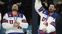 Auston Matthews (34) of the United States and Connor Hellebuyck (37) of the United States celebrate their gold medals against Canada in the men's ice hockey gold medal game during the Milano Cortina 2026 Olympic Winter Games at Milano Santagiulia Ice Hockey Arena.
