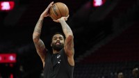 Mavericks guard D'Angelo Russell (5) warms up before a game against the Portland Trail Blazers at Moda Center with the Bucks logo and Marc Stein in the background