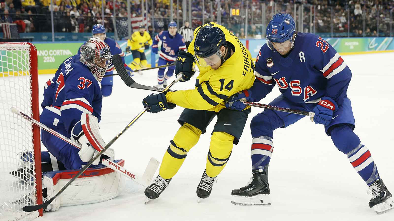 Joel Eriksson Ek (14) of Sweden battles for the puck between Connor Hellebuyck (37) of the United States and Charlie McAvoy (25) of the United States in a men's ice hockey quarterfinal during the Milano Cortina 2026 Olympic Winter Games at Milano Santagiulia Ice Hockey Arena. 