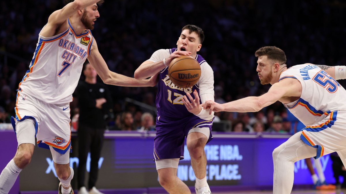 Lakers forward Jake LaRavia (12) is defended by Oklahoma City Thunder center Chet Holmgren (7) and center Isaiah Hartenstein (55) during the third quarter at Crypto.com Arena with Pistons logo in the background