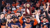 Illinois Fighting Illini head coach Brad Underwood and players celebrate with the trophy on the podium after defeating the Iowa Hawkeyes in an Elite Eight game of the South Regional of the men's 2026 NCAA Tournament at Toyota Center.