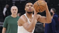 Milwaukee Bucks forward Giannis Antetokounmpo (34) shoots during pregame warmups as his personal trainer Michael Kalavros looks on from the back left before a game against the LA Clippers at Fiserv Forum.