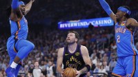 Lakers guard Luka Doncic (77) drives between Oklahoma City Thunder guard Luguentz Dort (5) and guard Shai Gilgeous-Alexander (2) during the first quarter at Paycom Center with Thunder coach Mark Daigneault in the background