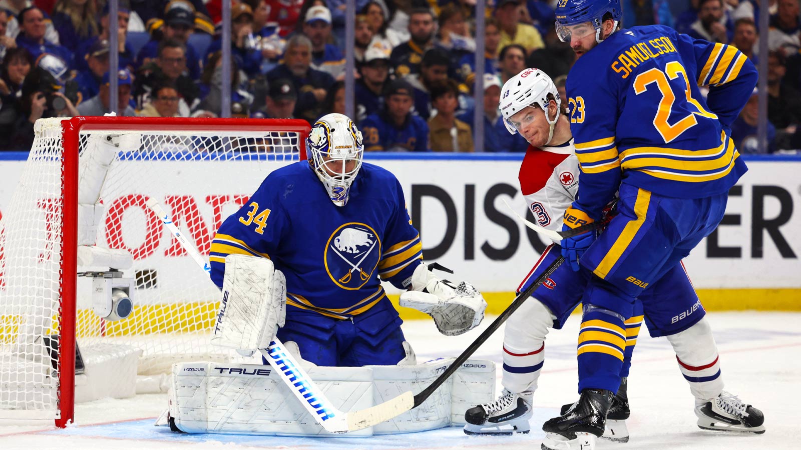 Buffalo Sabres defenseman Mattias Samuelsson (23) and Montréal Canadiens right wing Cole Caufield (13) look for the puck as Buffalo Sabres goaltender Alex Lyon (34) looks to make a save during the third period in game one of the second round of the 2026 Stanley Cup Playoffs at KeyBank Center.