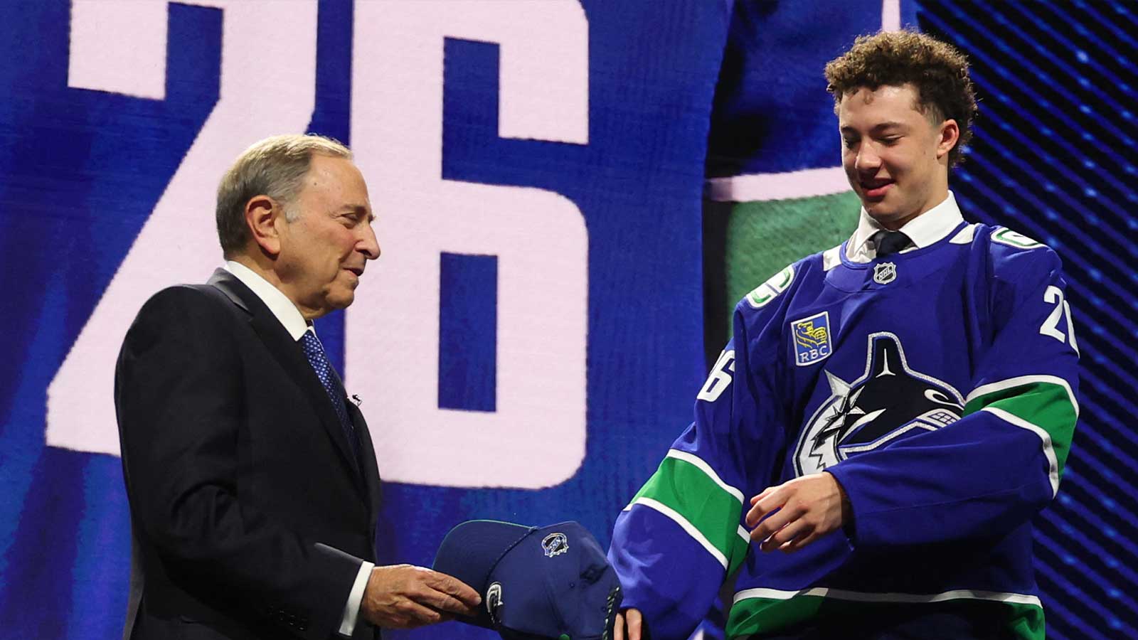 USA; Caleb Malhotra reacts with NHL commissioner Gary Bettman after being selected with the third pick in the first round of the 2026 NHL Draft by the Vancouver Canucks at KeyBank Center. 