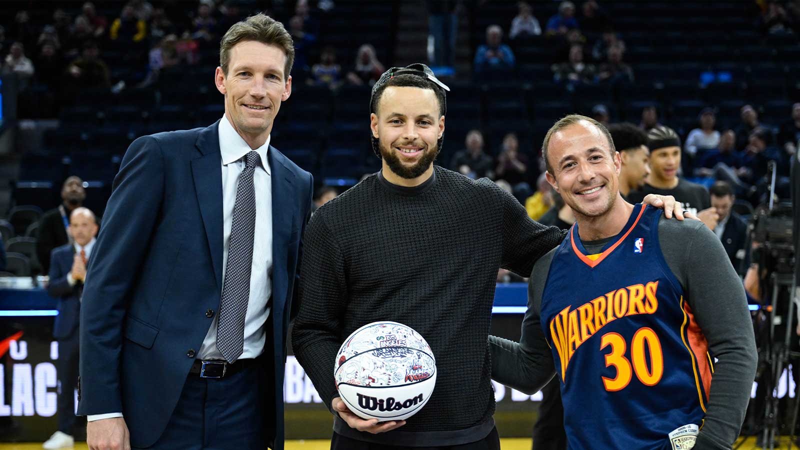 Golden State Warriors guard Stephen Curry, center, accepts a ball honoring his All-Star Game selection from Golden State Warriors general manager Mike Dunleavy, left, and 12-year season ticket member Casey Kaminsky, right, before the game against the San Antonio Spurs at Chase Center.